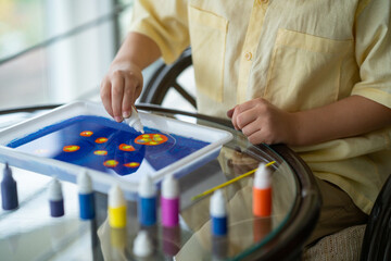 Drawing on water using the ebru technique. Creative development of children. Art therapy with kids. A boy in a yellow shirt draws with water paints
