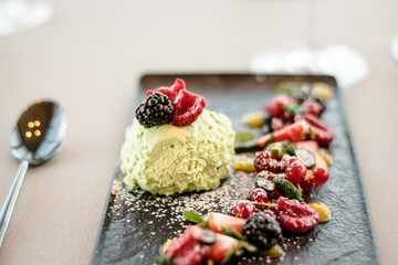 Ice cream on a black plate with fruits and sauce at a restaurant
