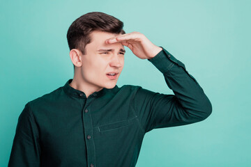 Portrait of a young man hesitate looking away with hand head on teal background