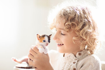 Child playing with kitten. Cat and kid at home.