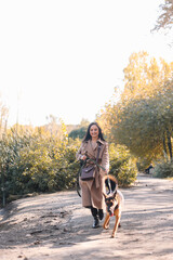 A happy funny girl in a casual coat walks with her dog, pet and best friend in the autumn forest by the water in nature in fall outdoor, selective focus