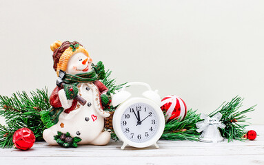 On a light background, a beautiful snowman, a white alarm clock and fir-tree branches with New Year's balls and gifts. Christmas concept. Copy space.