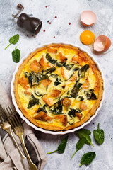 Homemade quiche tart with red fish and spinach on light wooden background. Vintage style. Top view