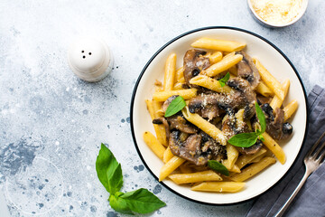 Penne rigate pasta with mushrooms, parmesan cheese and basil leaves in ceramic dish on light old...