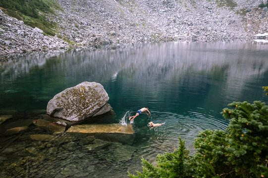Male hiker diving into alpine lake with dog