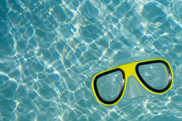 A yellow snorkel swimming goggles floating in a clear blue rippled swimming pool