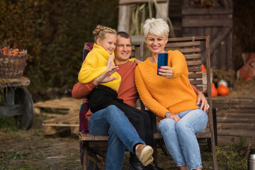 Fototapeta na wymiar Beautiful young family sitting in wooden sun loungers for a picnic, enjoying an autumn day in the park, makes a selfie