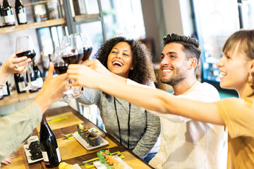 Multicultural smiling friends toasting red wine at sushi bar restaurant - Food lifestyle concept with young people having fun together at all you can eat buffet - Vivid filter with focus on guy face
