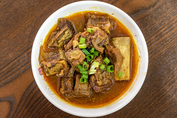 The beef dish is in the plate on the wooden table