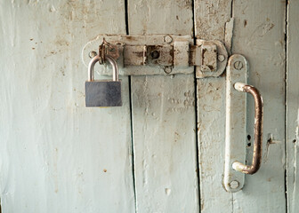 Painted, dirty wooden door with metal handle, latch and padlock, in a country house. 