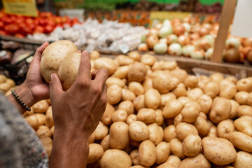 manos de un hombre moreno tomando papas de un cajón en una verdulería