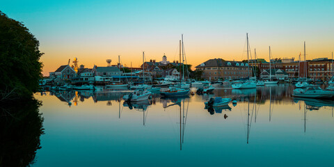 Fototapeta na wymiar Tranquil sunrise seascape with moored boats and yachts at the marina in Woods Hole, Massachusetts. Blue ocean and sky with orange reflections of the daybreak.
