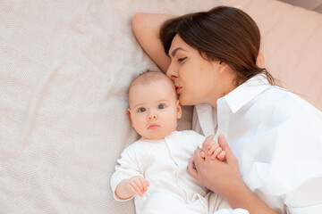 mom and baby are lying in the bedroom on the bed kissing on the cheek