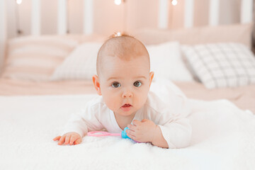 a baby in a white jumpsuit is lying on a bed with a rattle at home