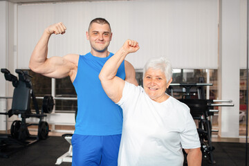 Happy smiling people are engaged in physical education, simulators in gym. Active healthy lifestyle, senior concept. A woman with gray hair, a young coach is a muscular man. power