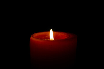 Round red candle on a black background. Burning candle on a black background.
