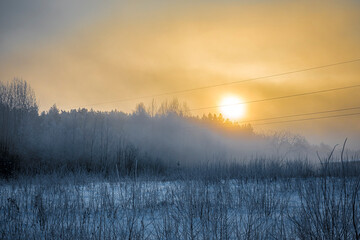 Misty sunrise on the outskirts of Vilnius, Lithuania. Orange dawn, fog over a field, cold air and romantic December mood. Selective focus on the forest, blurred background.