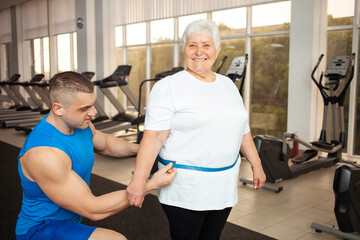 trainer measures the volume, waist, centimeters of the body. An elderly woman lost weight in the...