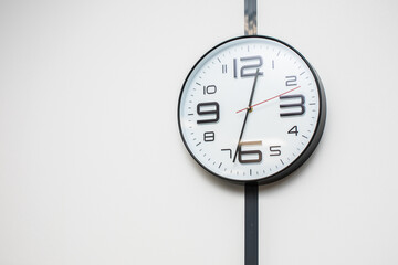 Minimalistic photo of a modern white clock with large numbers hanging on a white wall in the office
