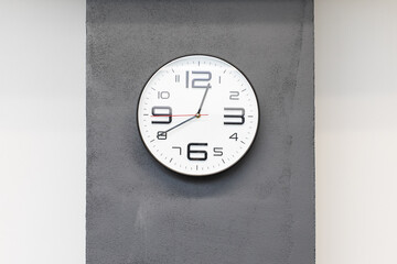 Minimalistic photo of a modern white clock with large numbers hanging on a grey wall in the office