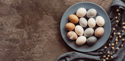 Blue plate with Easter eggs and a feather on a concrete background. Top view with copy space.
