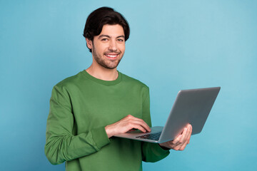Portrait of cheerful young good looking businessman working in laptop start-up project isolated on blue color background