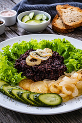 Fried blood sausage with onion, lettuce and cucumber on wooden table
