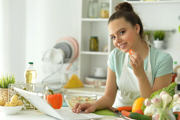 Portrait of beautiful young woman making salad in kitchen