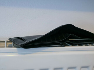 Man's synthetic empty leather wallet on white radiator , conceptual image of increasing energy prices, focus on the left side of the wallet.