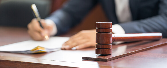 Closeup of judge wooden gavel on sounding block and man handwriting on the background. The legal...
