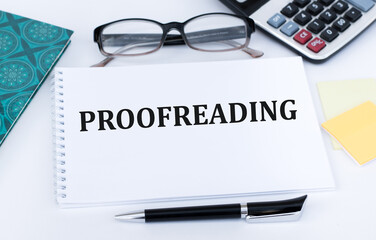 Text Proofreading on a white notebook on the table next to the calculator, glasses, pen