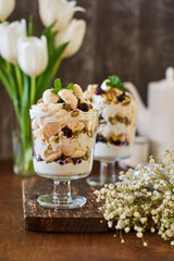 Eton Mess. Trifle with meringue, blueberries, pistachios and mint. Dessert in a glass. Side view. Wooden background.
