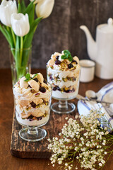 Eton Mess. Trifle with meringue, blueberries, pistachios and mint. Dessert in a glass. Side view. Wooden background.
