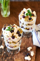 Eton Mess. Trifle with meringue, blueberries, pistachios and mint. Dessert in a glass. Side view. Wooden background.