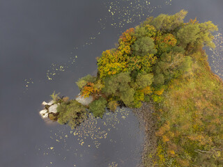 Drone nature photography taken from above in Sweden in fall time. Bird's eye view of a lake with trees in autumn colors. Dark water surface background, copy space and place for text.