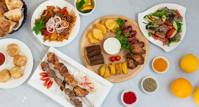 oriental cuisine, barbecue, manti, sausage snacks, salad, fried potatoes on a white table decorated with spices and lemons