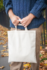 Stylish man holding white blank canvas tote shopping bag