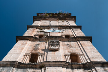 The tall bell tower is a symbol of Perast. A stone clock tower overgrown with grass and flowers....
