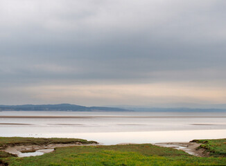 view of the coast at grange over sands in cumbria with grass covered wetland in the foregrounds and the north lakes area in the distance
