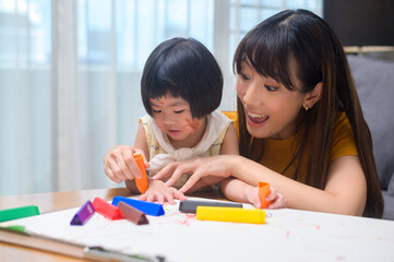 Young mom helping daughter drawing with colored pencils in living room at home.