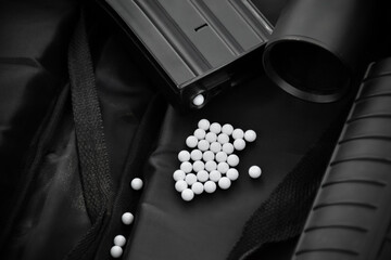 Airsoft gun with round white plastic bullets on a black leather background. Soft and selective...