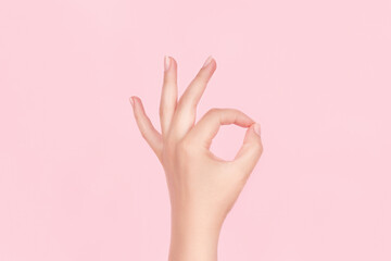 Female hand with beautiful manicure - pink nude nails making ok sign on pink background. Nail care concept