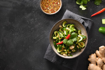 Asian spicy broken cucumbers salad with cilantro, ginger, pepper chili, black vinegar on black background. Copy space. Spicy cucumbers. Traditional cold Chinese and Vietnam appetizer. Top view.