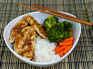 Teriyaki chicken bowl with rice, broccoli, carrots and vegetables with chopsticks.
