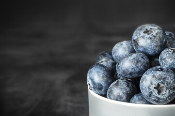 Fresh juicy blueberries in the bowl on the black background.