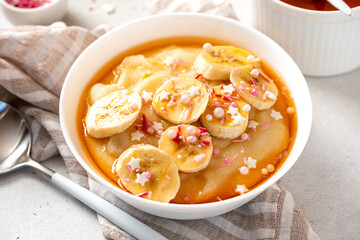 Semolina porridge with syrup and banana. Sweet breakfast, baby food. Semolina porridge in a white bowl on a gray concrete background.