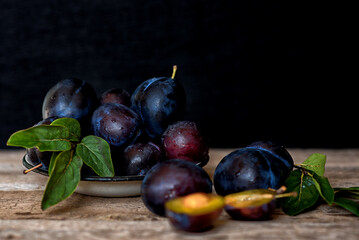 Ripe plum with green leaves on rustic background. Ripe fresh organic plums.