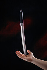 The concept of hand holding a large knife blade upwards diagonally on black background.