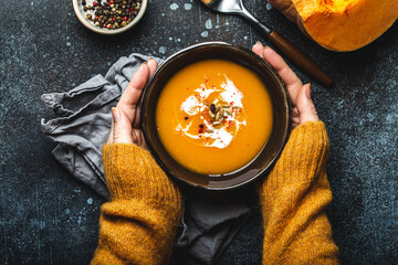 Female hands with bowl of pumpkin soup - obrazy, fototapety, plakaty