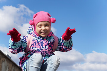 Funny little girl on a background of blue sky. Scares people. Pink clothes. Child laughing in the street.